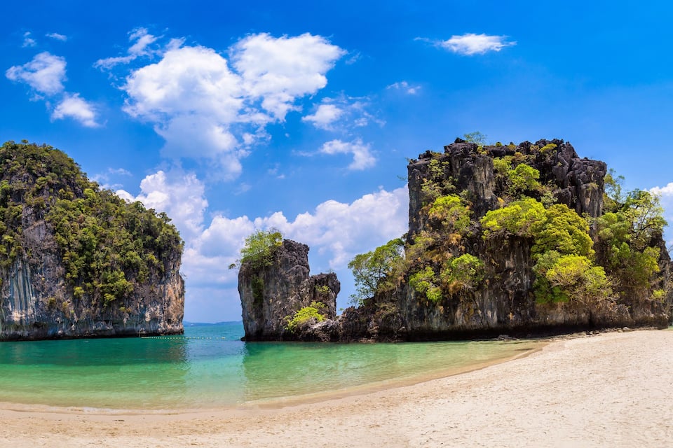 A beach with clear turquoise waters, white sand, and rocky cliffs with lush greenery.