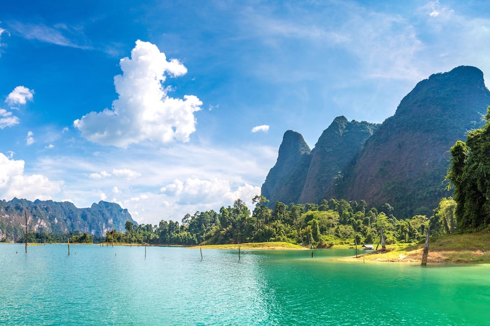 A turquoise lake surrounded by forested hills and a clear sky.