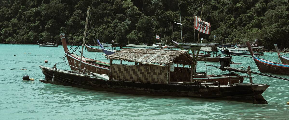 A traditional boat docked at a turquoise beach with a forested hill in the background.