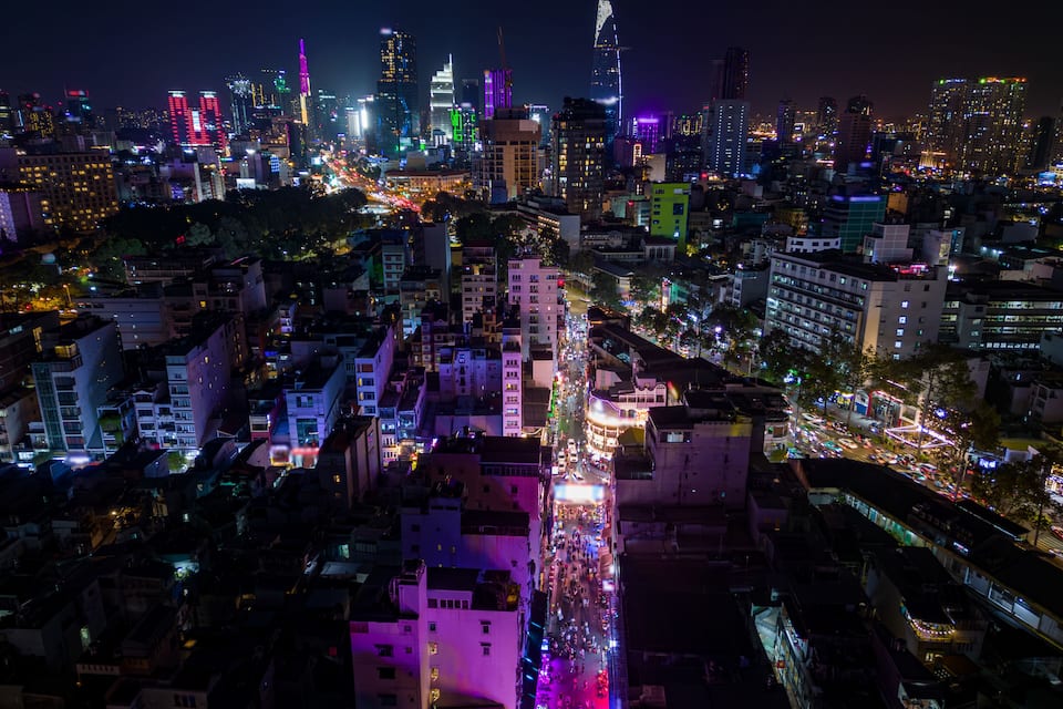 Paisagem urbana noturna com edifícios iluminados e ruas movimentadas.