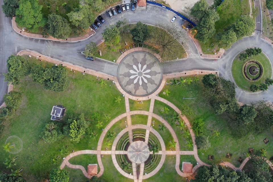 Vue aérienne d’un rond-point dont le parterre central est aménagé en forme de fleur, entouré de verdure et de quelques voitures garées.