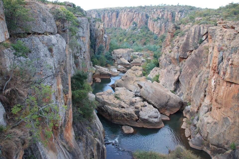 Um cânion com um rio serpenteando por ele, cercado por penhascos rochosos e vegetação escassa.