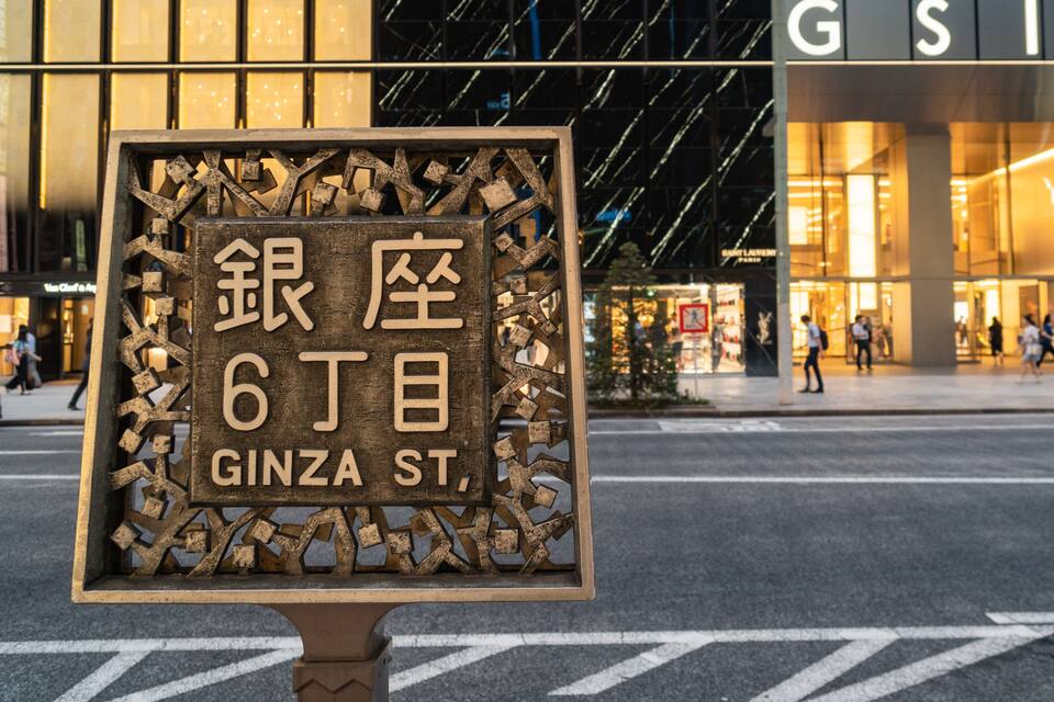 Un letrero con caracteres japoneses y la frase 'GINZA ST.' en inglés, frente a un edificio con 'GSX' en la fachada.