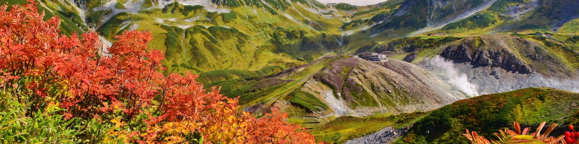 A mountainous landscape with green valleys and red foliage.