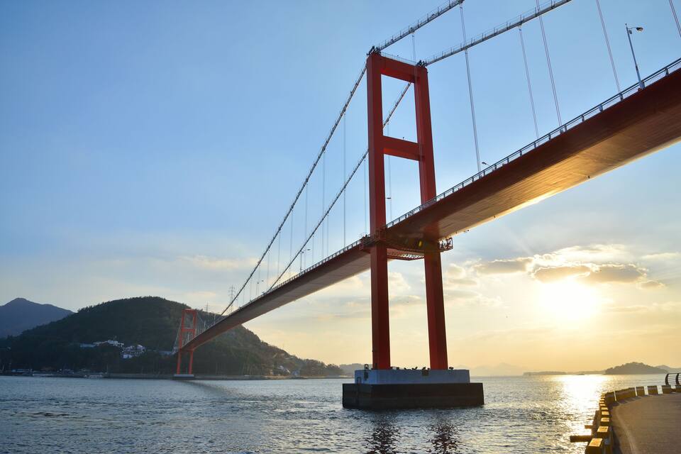 Un puente colgante rojo sobre un cuerpo de agua, con montañas al fondo.