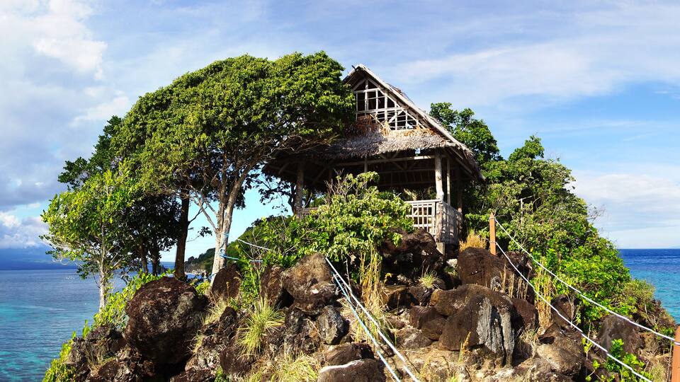 A wooden house on a rocky island surrounded by ocean.