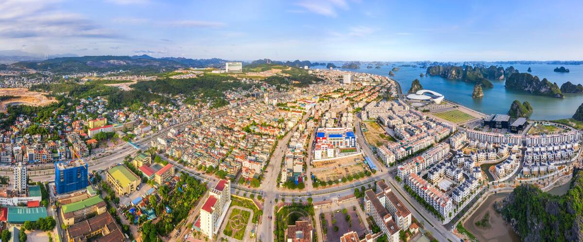 A coastal cityscape with dense urban development, a prominent modern building, and a river with rocky islands.