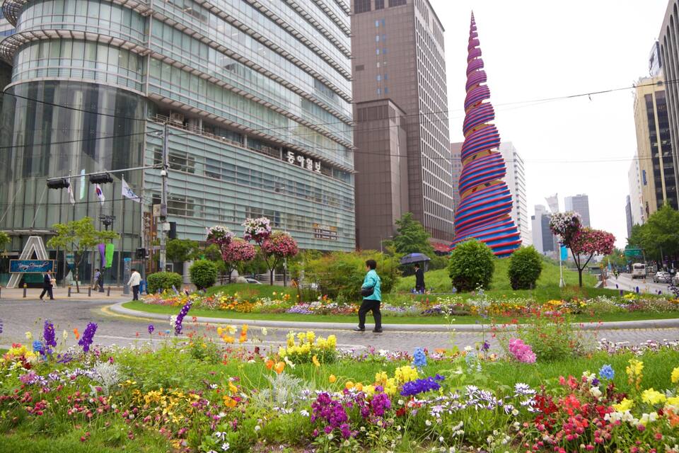 A cityscape with modern buildings, a distinctive spiral tower, and a vibrant flower garden.
