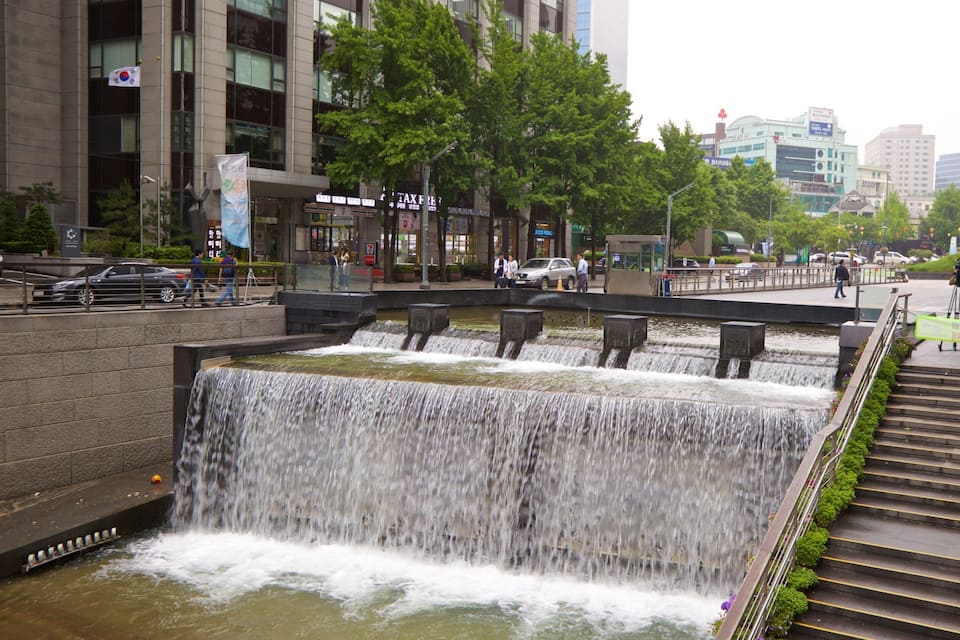 Una cascada escalonada en un entorno urbano, con edificios modernos y una escultura colorida al fondo.