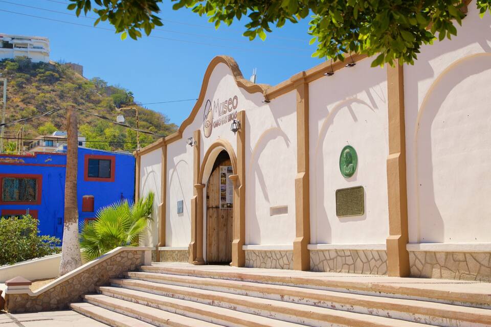 A white building with a sign reading "Museo Casa San Lucas" and a wooden door.