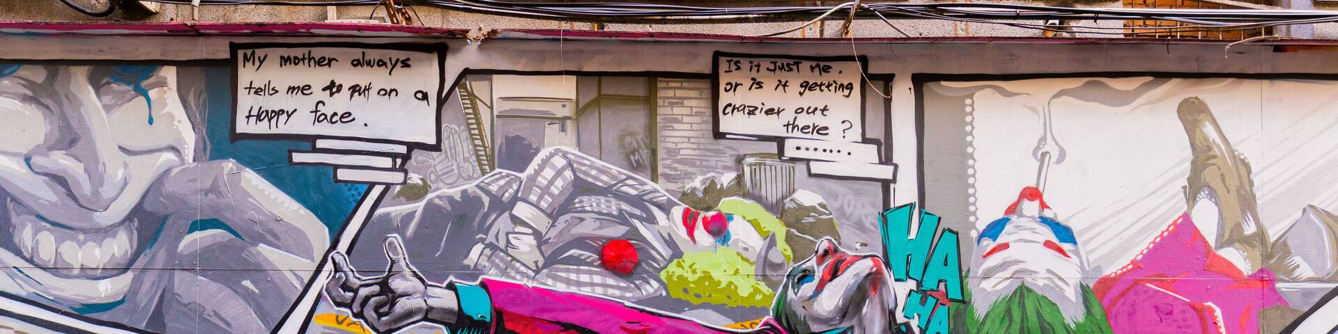 A colorful street mural with graffiti art, including a figure with a red cape and the word "HA HA" repeated.