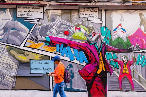 Ein farbenfrohes Wandgemälde mit Graffiti-Kunst, darunter eine Figur mit rotem Umhang und der mehrfach wiederholte Schriftzug "HA HA".