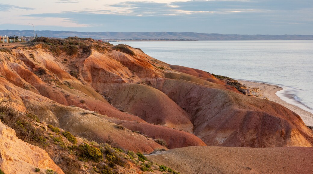 Un paisaje costero con acantilados rojizo-marrón, una playa de arena y un mar tranquilo.