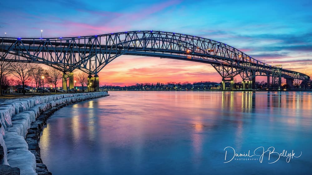 Eine Stahlbrücke überspannt einen zugefrorenen Fluss bei Sonnenuntergang.