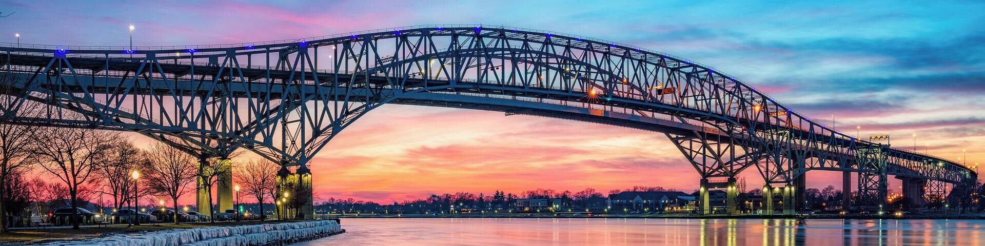 A steel bridge spanning a frozen river at sunset.