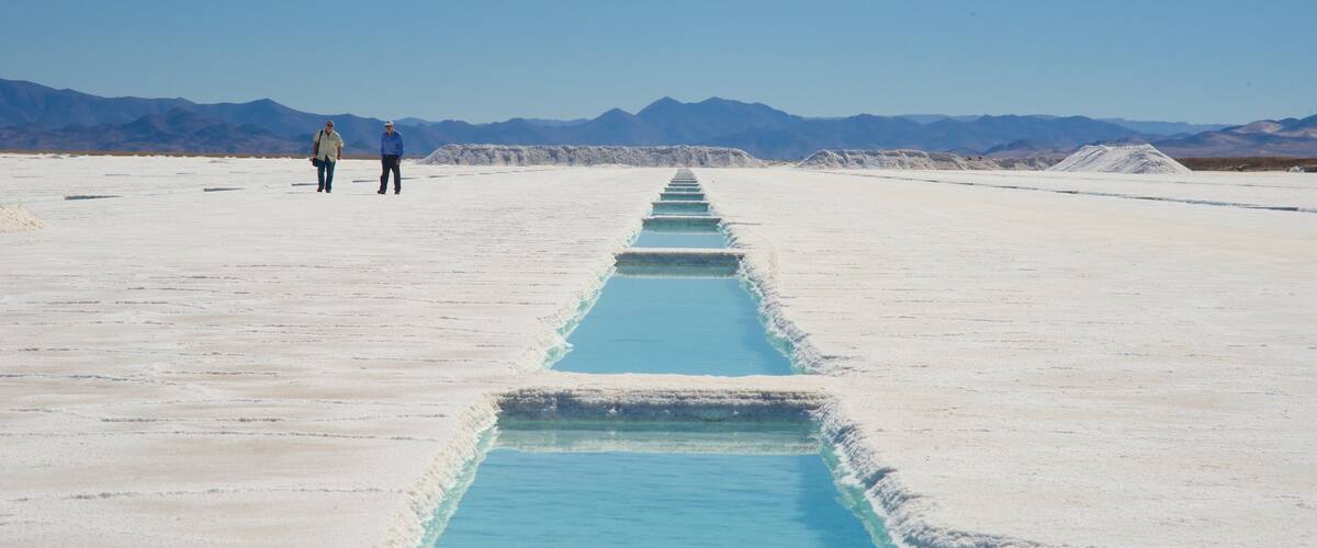 A salt flat with a blue water channel and mountains in the background.