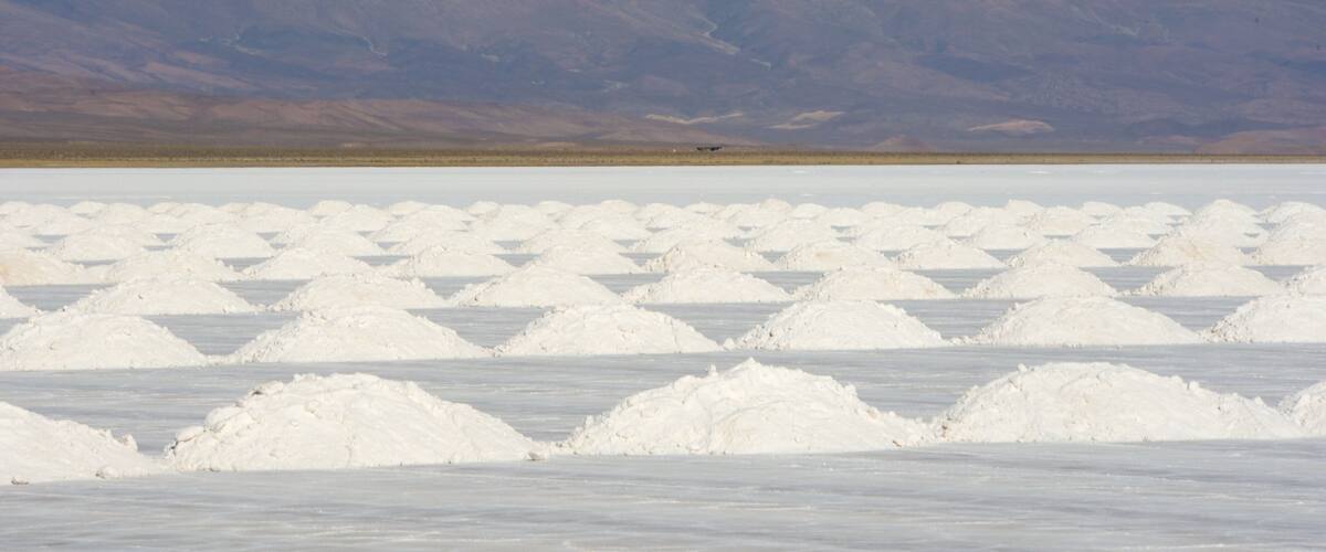 A salt flat with white salt formations and mountains in the background.