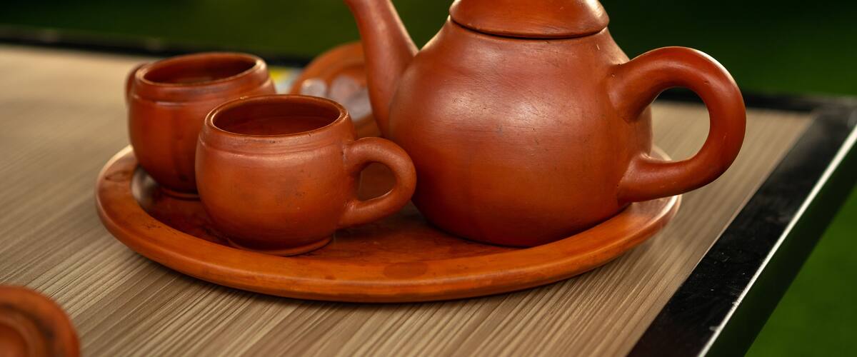 A traditional clay teapot and cups on a wooden tray.