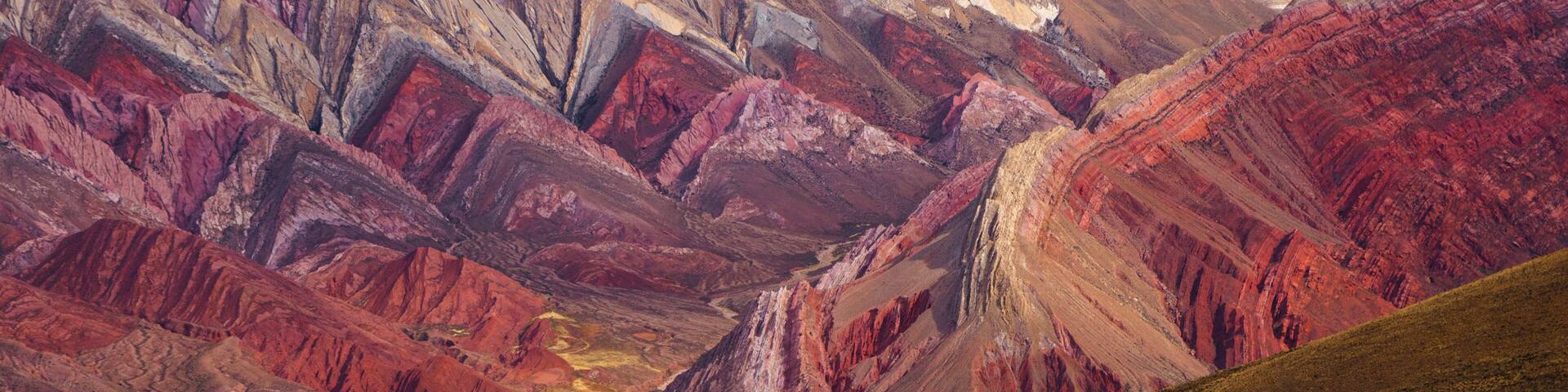 A mountainous landscape with red and brown hues, a clear blue sky, and a valley.