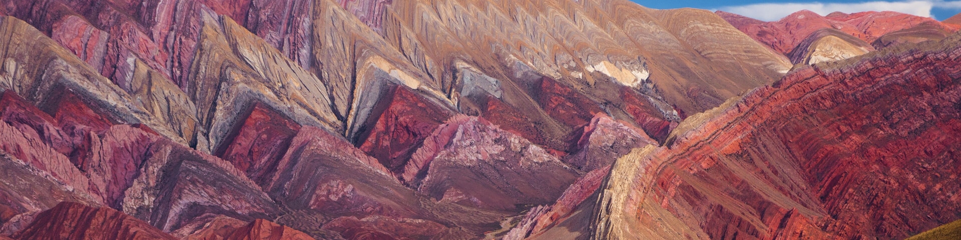 A mountainous landscape with red and brown hues, a clear blue sky, and a valley.