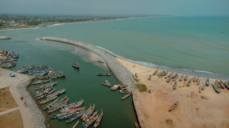 An aerial view of a coastal fishing village with numerous boats docked along the shore and a sandy beach.