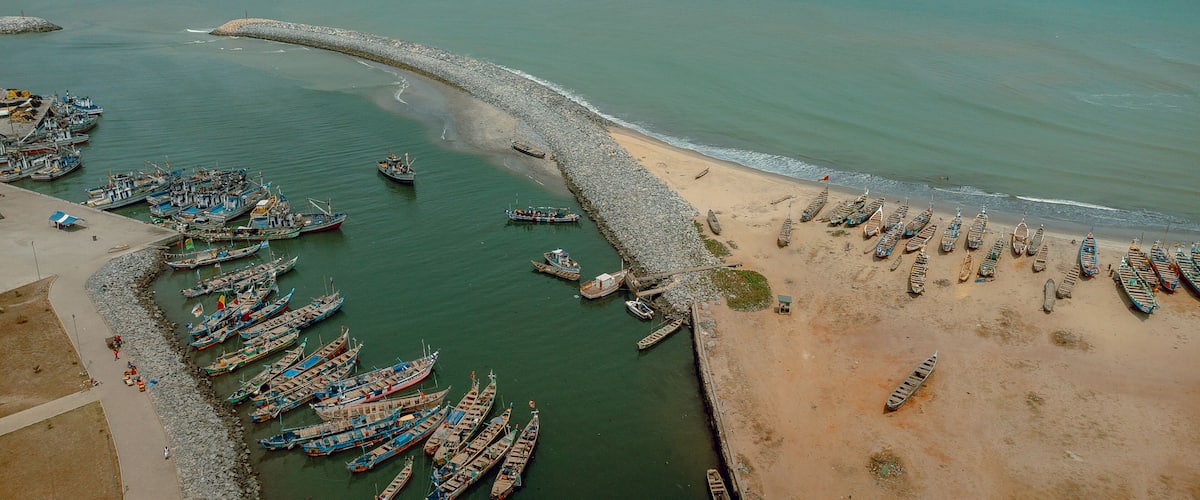 An aerial view of a coastal fishing village with numerous boats docked along the shore and a sandy beach.