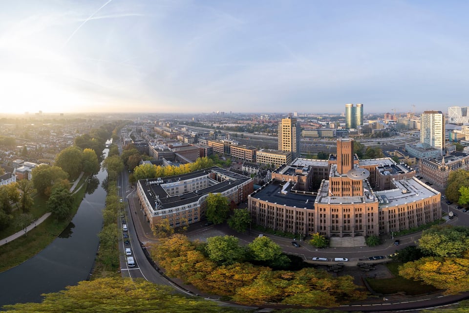 Vista panorámica de un paisaje urbano con un edificio circular destacado, rodeado de árboles y un río.