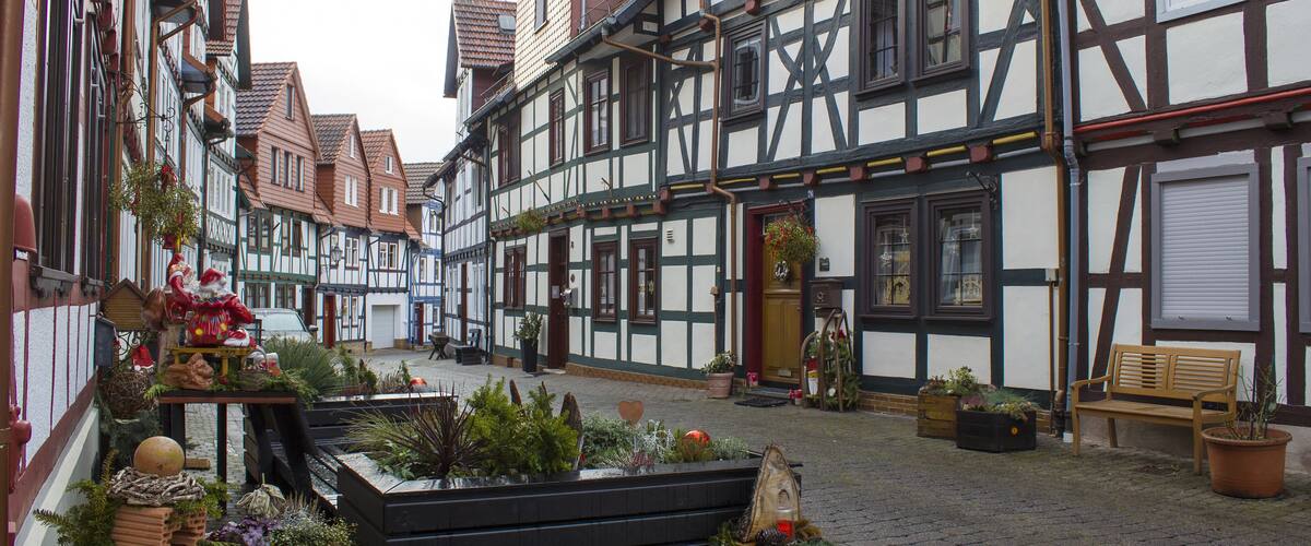 A cobblestone street with traditional half-timbered buildings, a wooden bench, and potted plants.