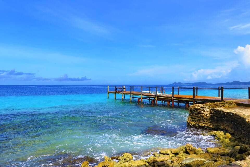A wooden pier extending into turquoise waters with clear skies.