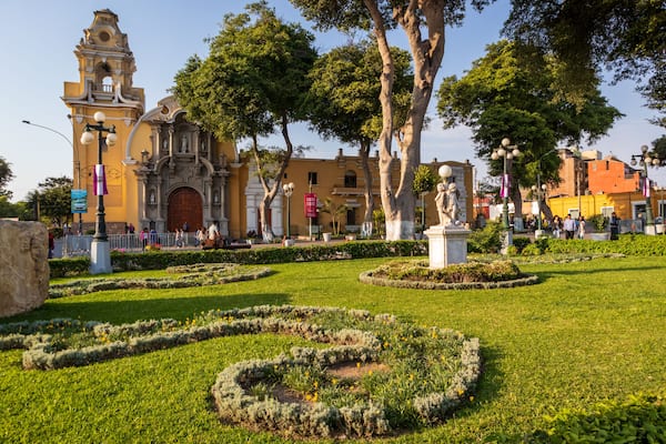 Um edifício histórico com uma torre de sino, rodeado por jardins bem cuidados e estátuas.