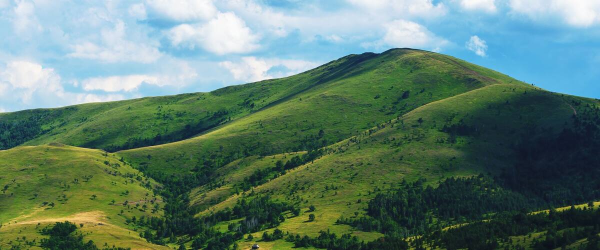 Rolling green hills with a prominent mountain peak under a partly cloudy sky.