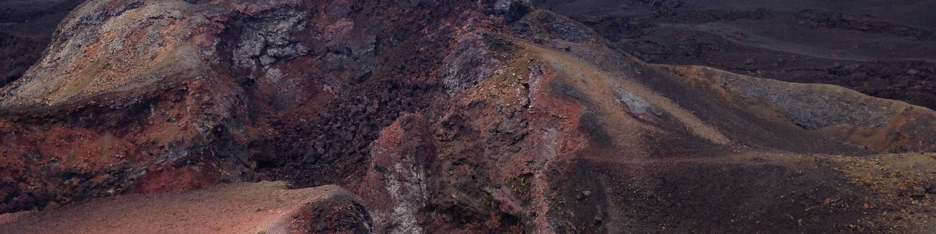 A volcanic landscape with reddish-brown soil and rocky formations.