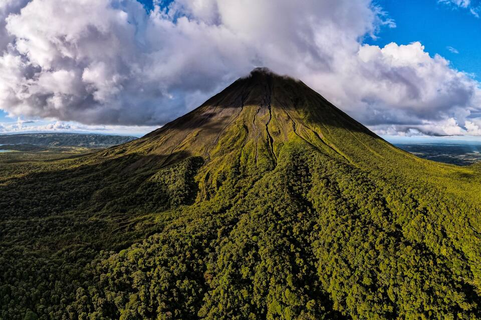 A volcano surrounded by dense forest and a lake.