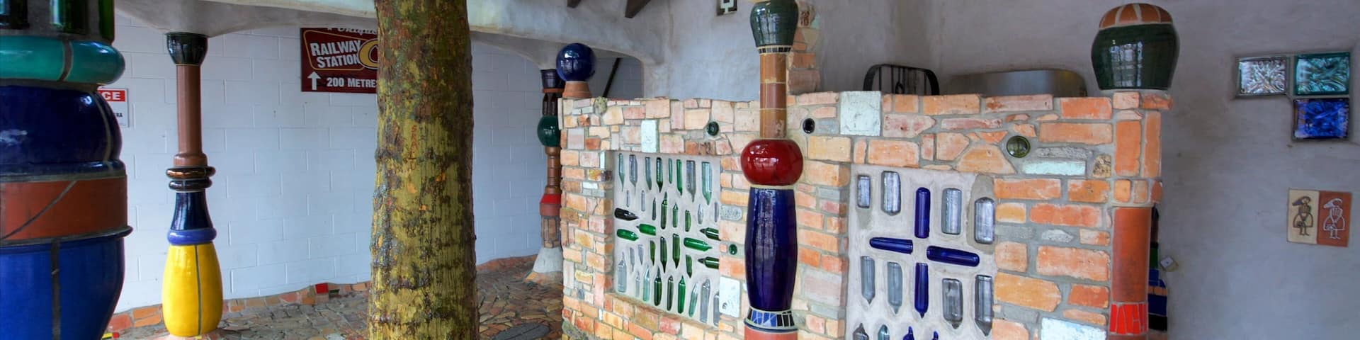 A rustic interior with a tree, colorful bottle-shaped columns, and a brick wall with bottle windows.