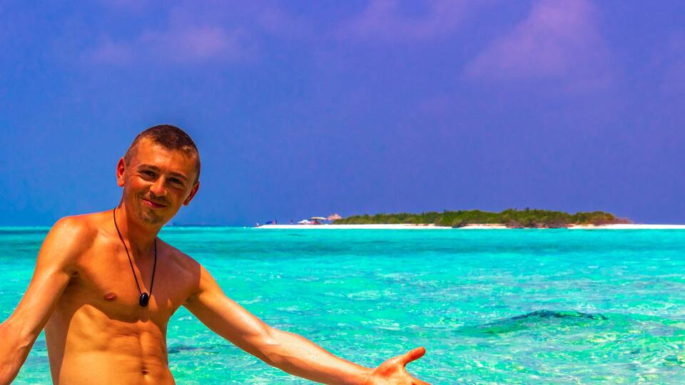 A man in a tropical setting with clear turquoise waters and a distant island.