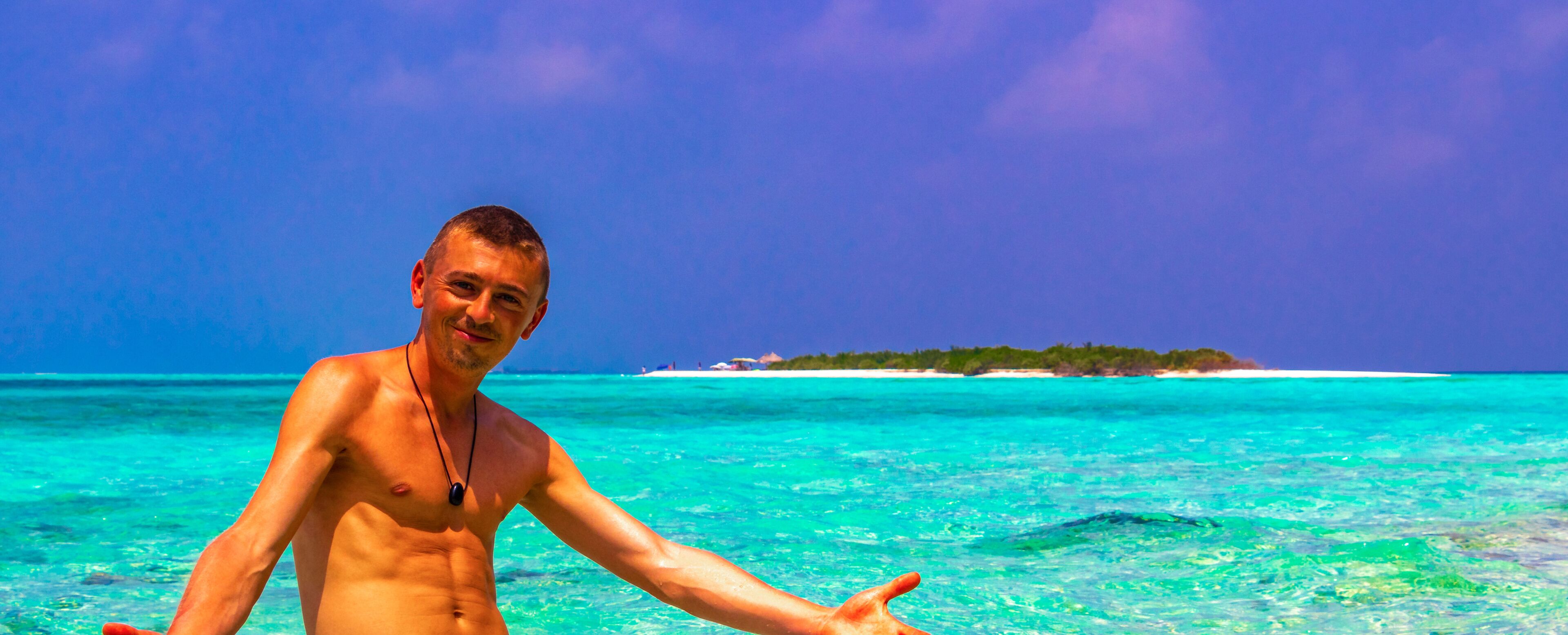 A man in a tropical setting with clear turquoise waters and a distant island.