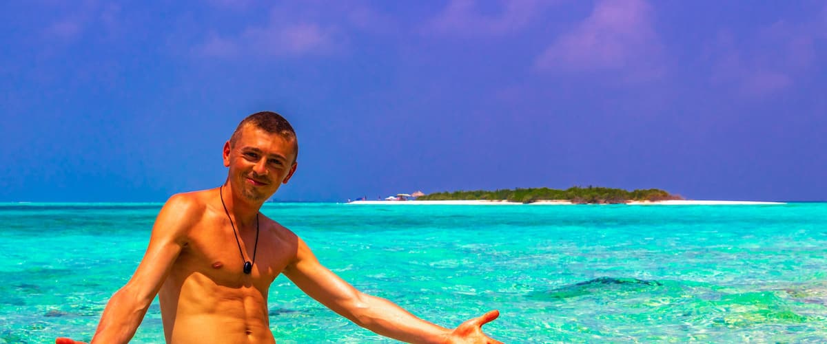 A man in a tropical setting with clear turquoise waters and a distant island.