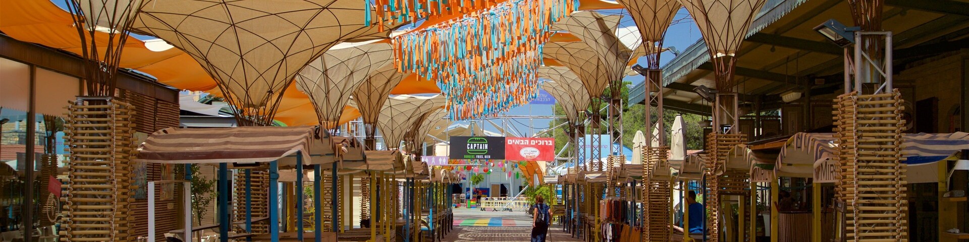 Un mercado al aire libre con mesas y sillas de madera, adornos colgantes y un suelo estampado.