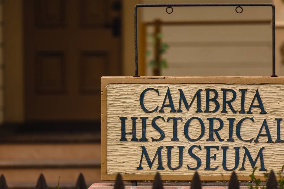 Uma placa de madeira com o texto "CAMBRIA HISTORICAL MUSEUM" fixada em uma estrutura metálica.