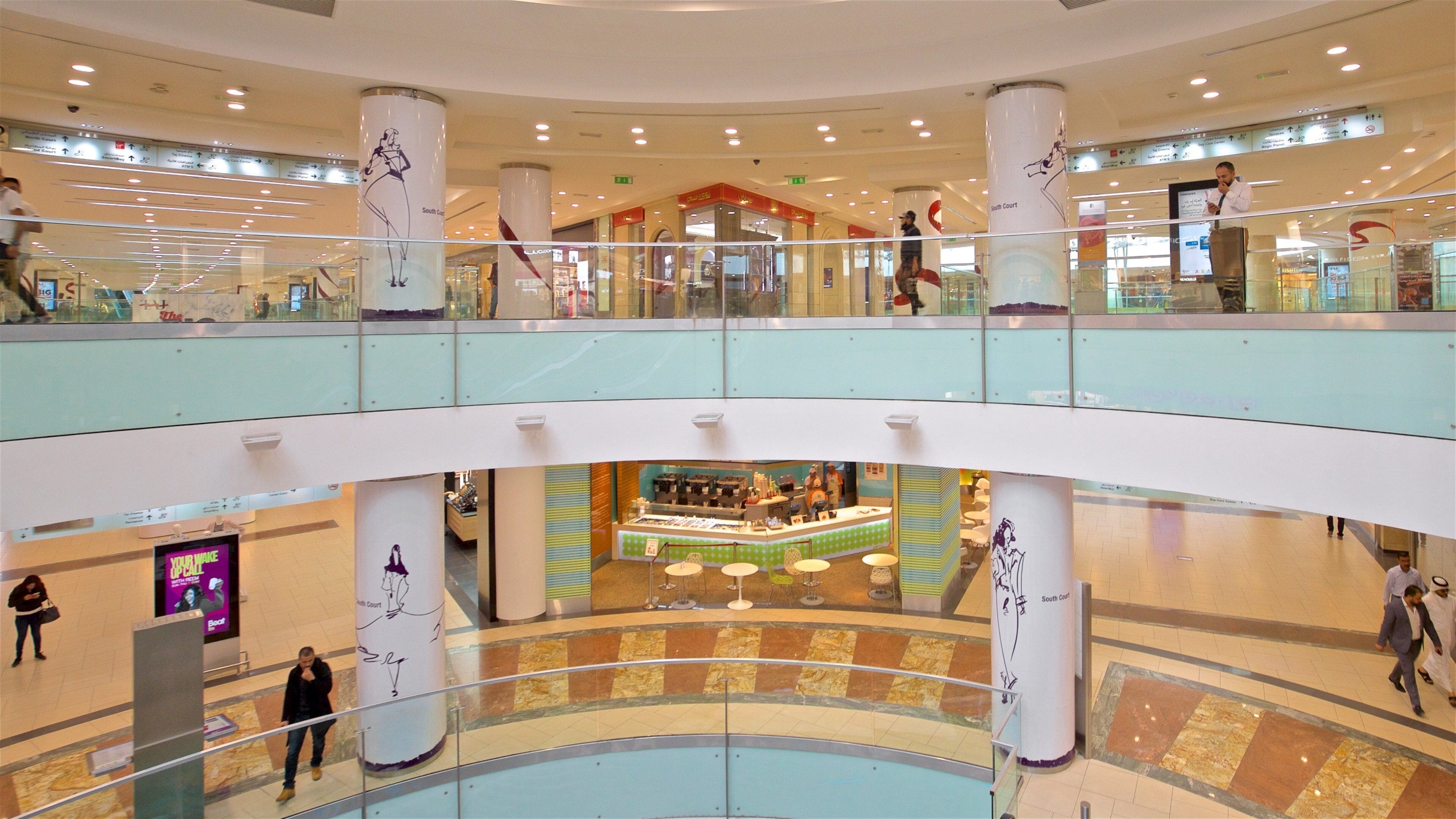 A multi-level shopping mall with glass railings, large columns, and a central food court.
