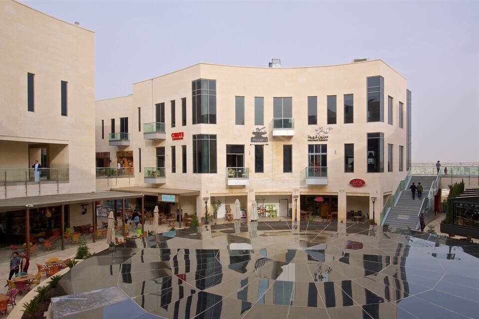 En modern byggnad med flera våningar, glasbeklädda balkonger och en central innergård med ett golv som reflekterar ljuset.