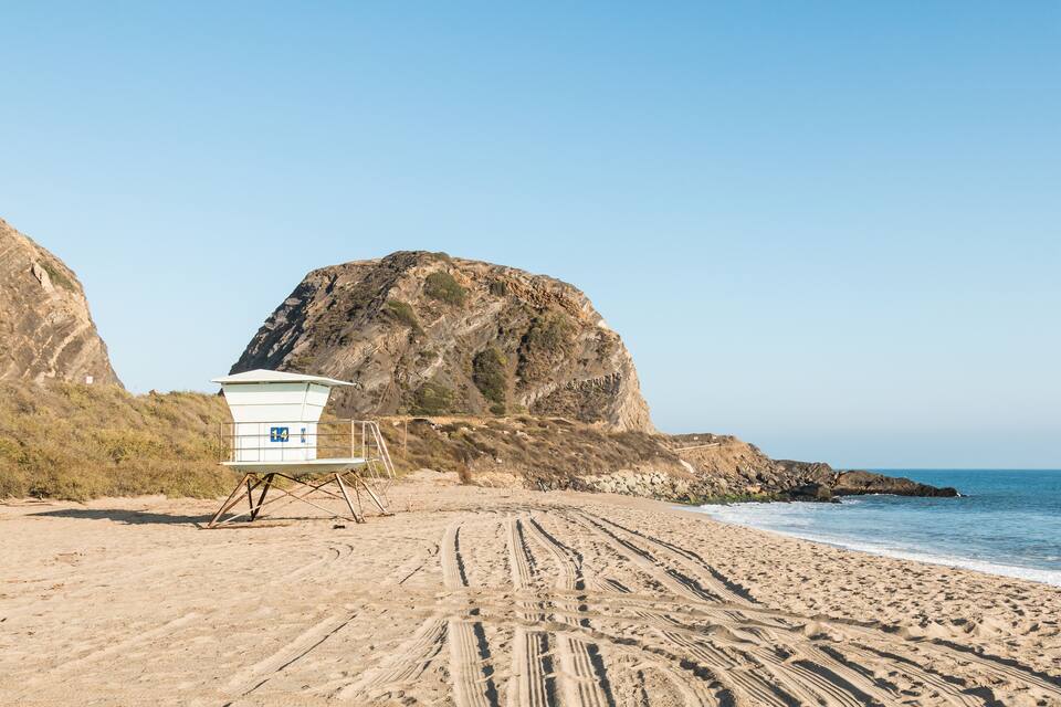 A beach with a lifeguard tower, sandy beach, and rocky cliffs.