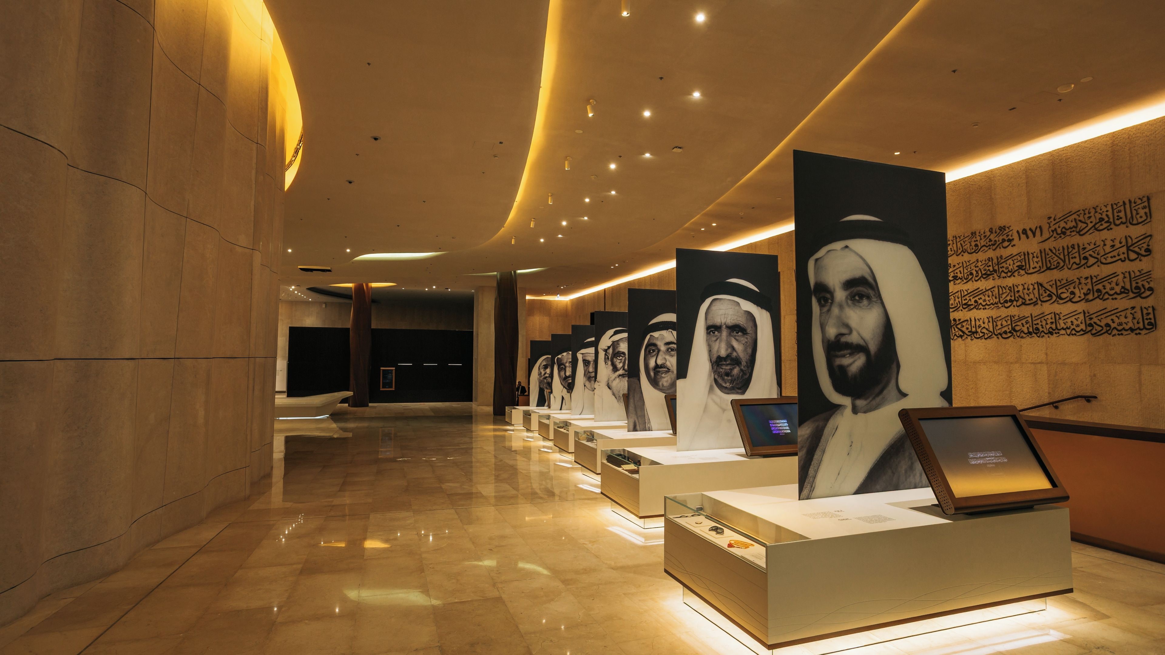 A corridor with a series of portrait displays and a reception desk.