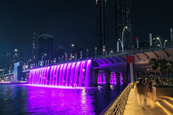 A nighttime cityscape with a bridge and a water feature with purple lighting.