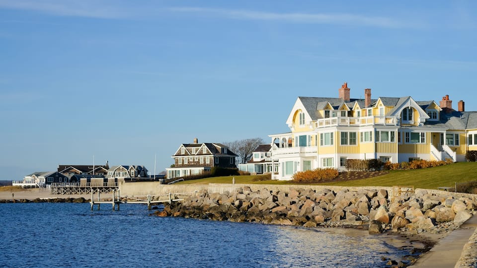 A waterfront property with a large house, a pier, and a rocky shoreline.