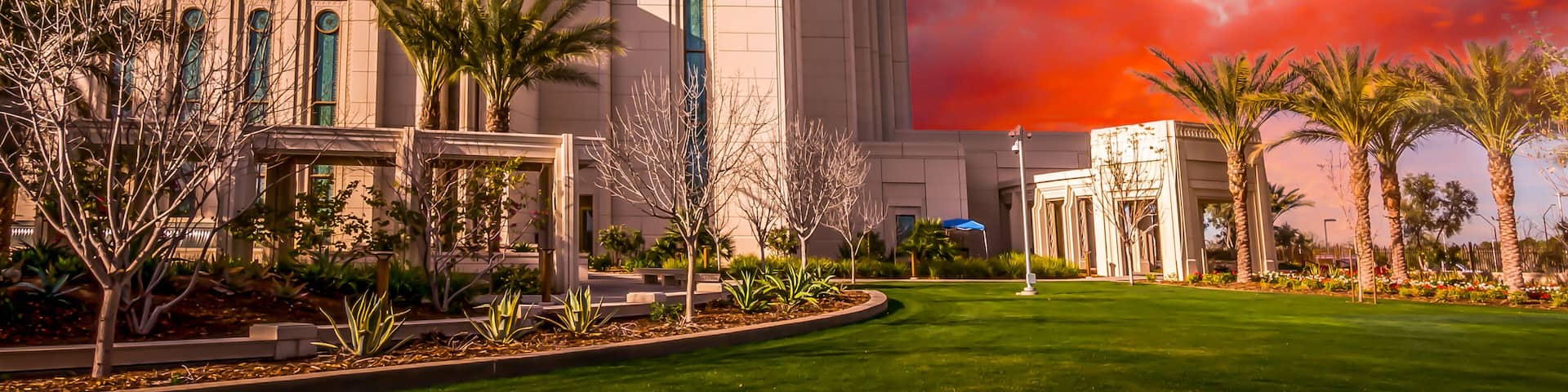 A large, modern building with a prominent spire, surrounded by well-maintained lawns and palm trees.