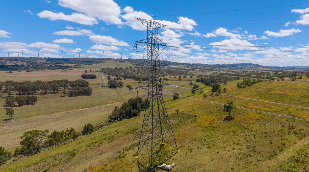 Une pylône de ligne électrique dans un paysage vallonné, avec des éoliennes visibles au loin.
