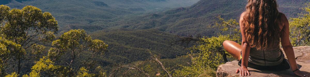 Woman sitting on cliff overlooking green mountains