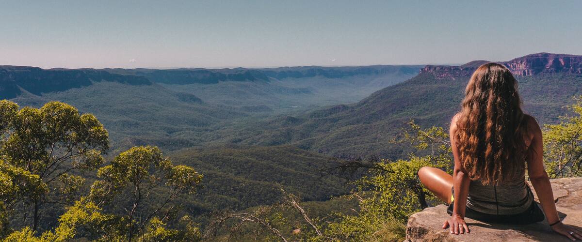 Woman sitting on cliff overlooking green mountains