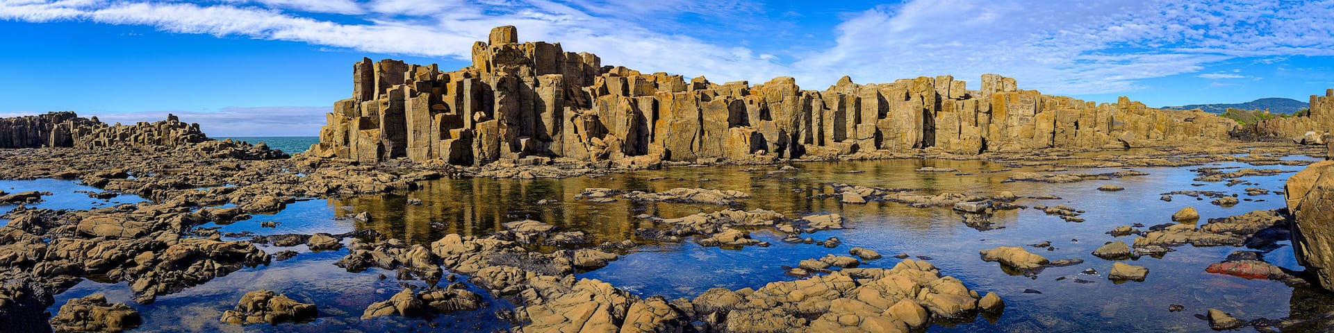 Panorama of basalt rock formations and rockpool reflections at Bombo Headland quarry, New South Wales coast, Australia